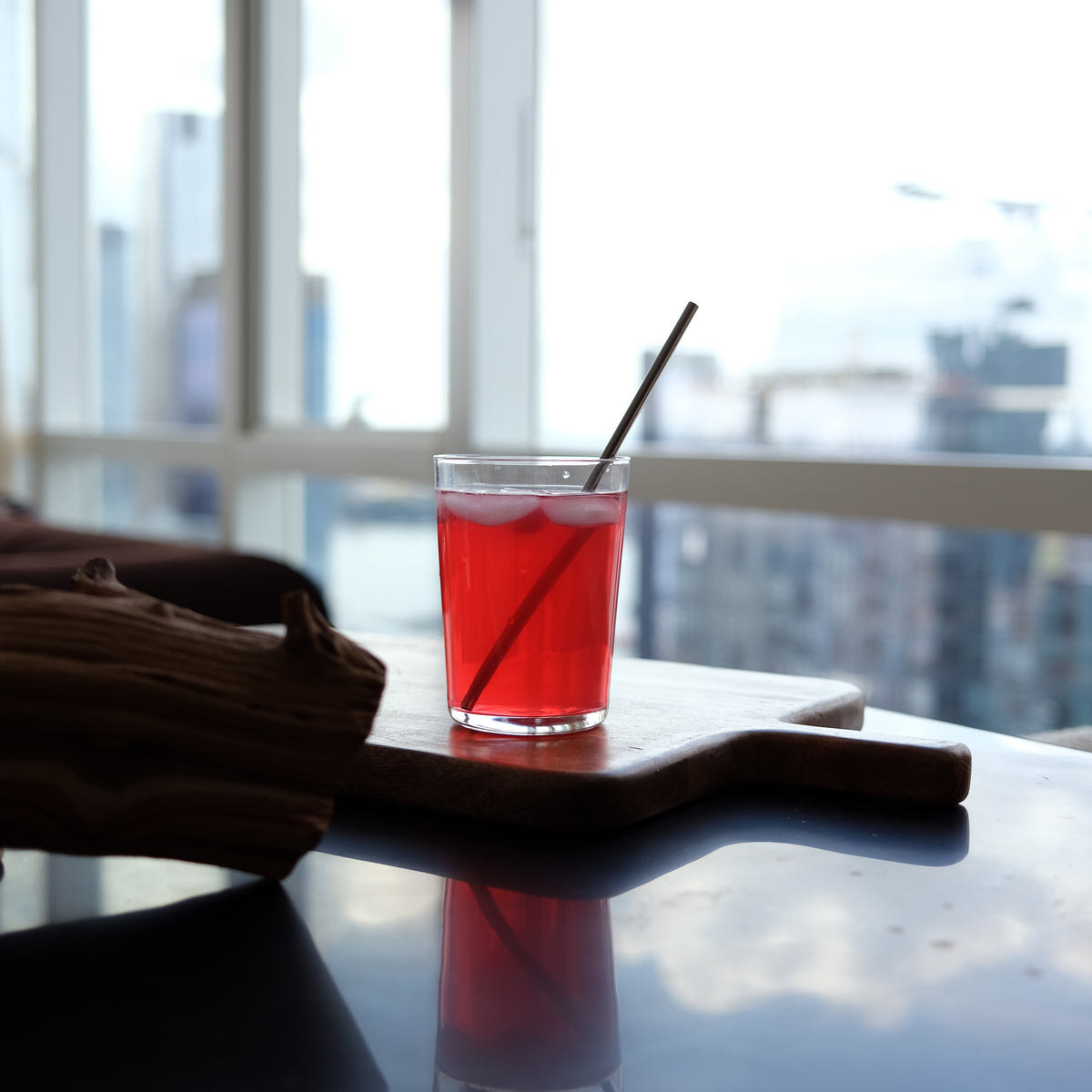Red drink with a straw in a glass on a table with a cityscape background