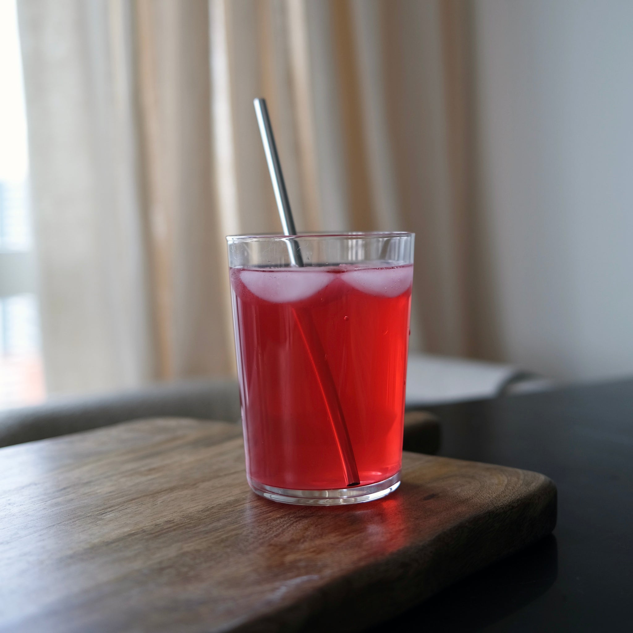 Glass of red drink with a straw on a wooden surface, blurred background