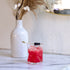Pink cocktail with berries in a Cassiopea DOF glass, next to a white vase with dried plants on a marble surface.