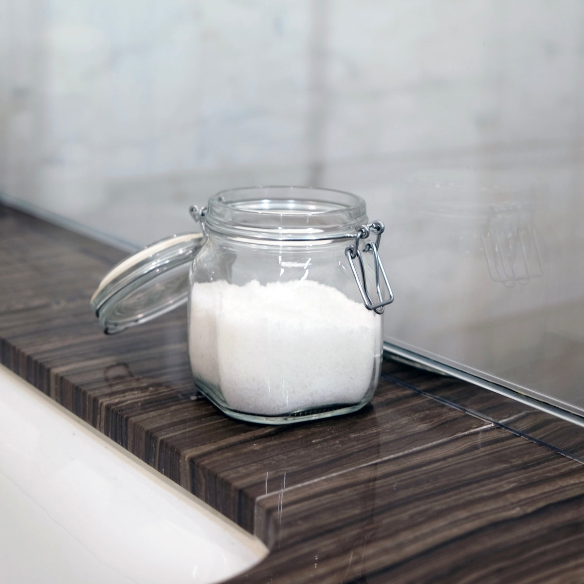 Clear glass jar with a lid containing white powder on a wooden surface.