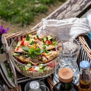 Picnic basket with salad in a Frigoverre Brillante bowl, drinks, and utensils on a grassy background.