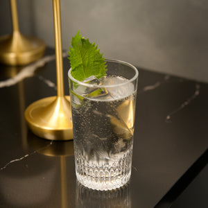 Clear glass with a cocktail and leaf on a dark surface with gold accents