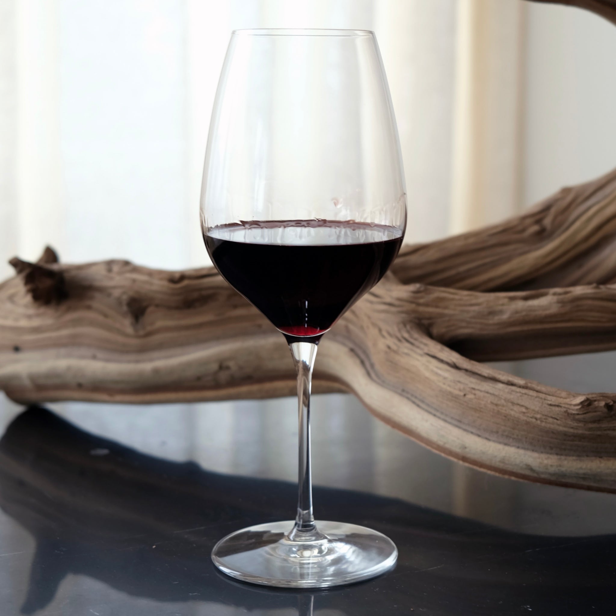 Wine glass with red wine on a dark surface with a wooden log in the background