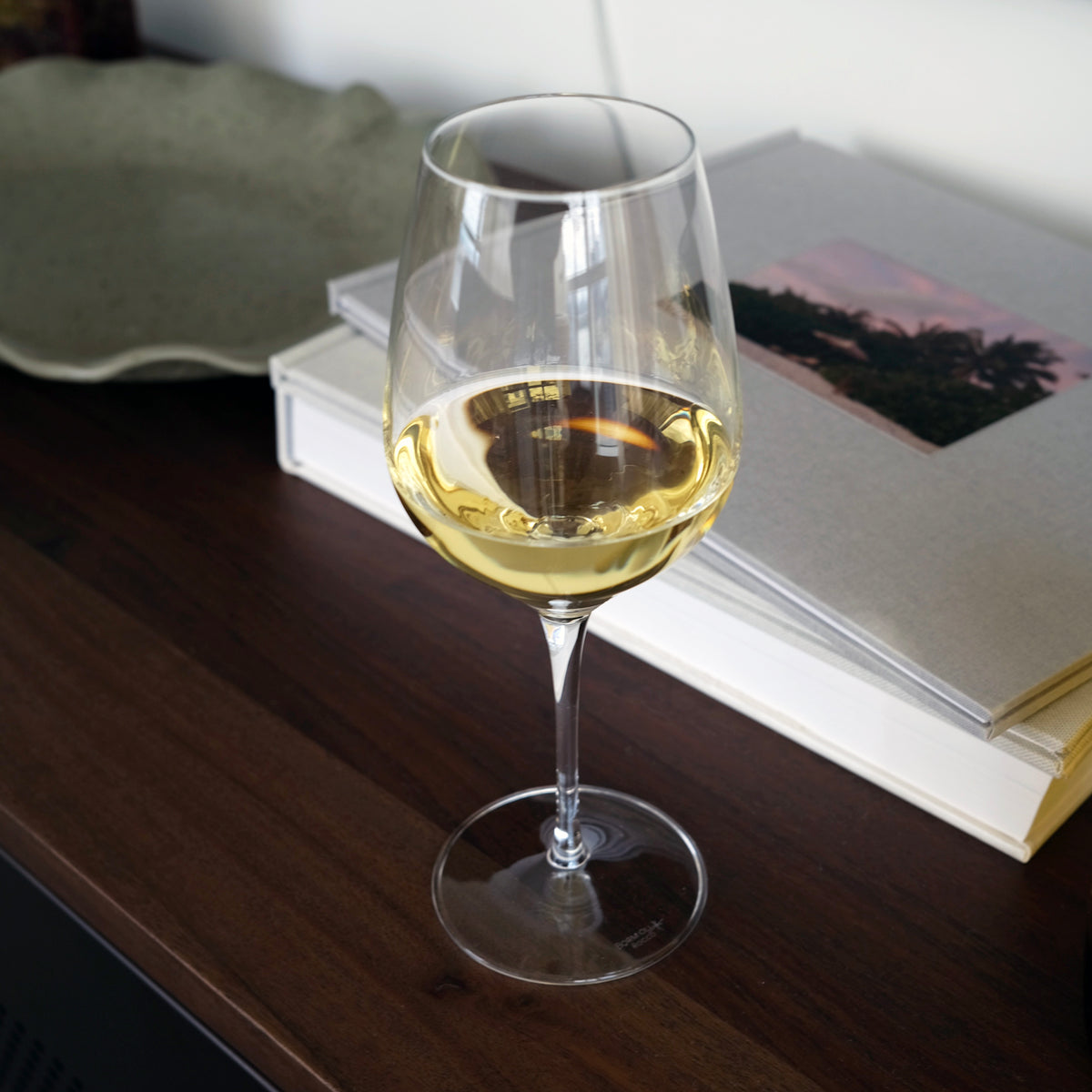 Wine glass with white wine on a wooden surface with books in the background
