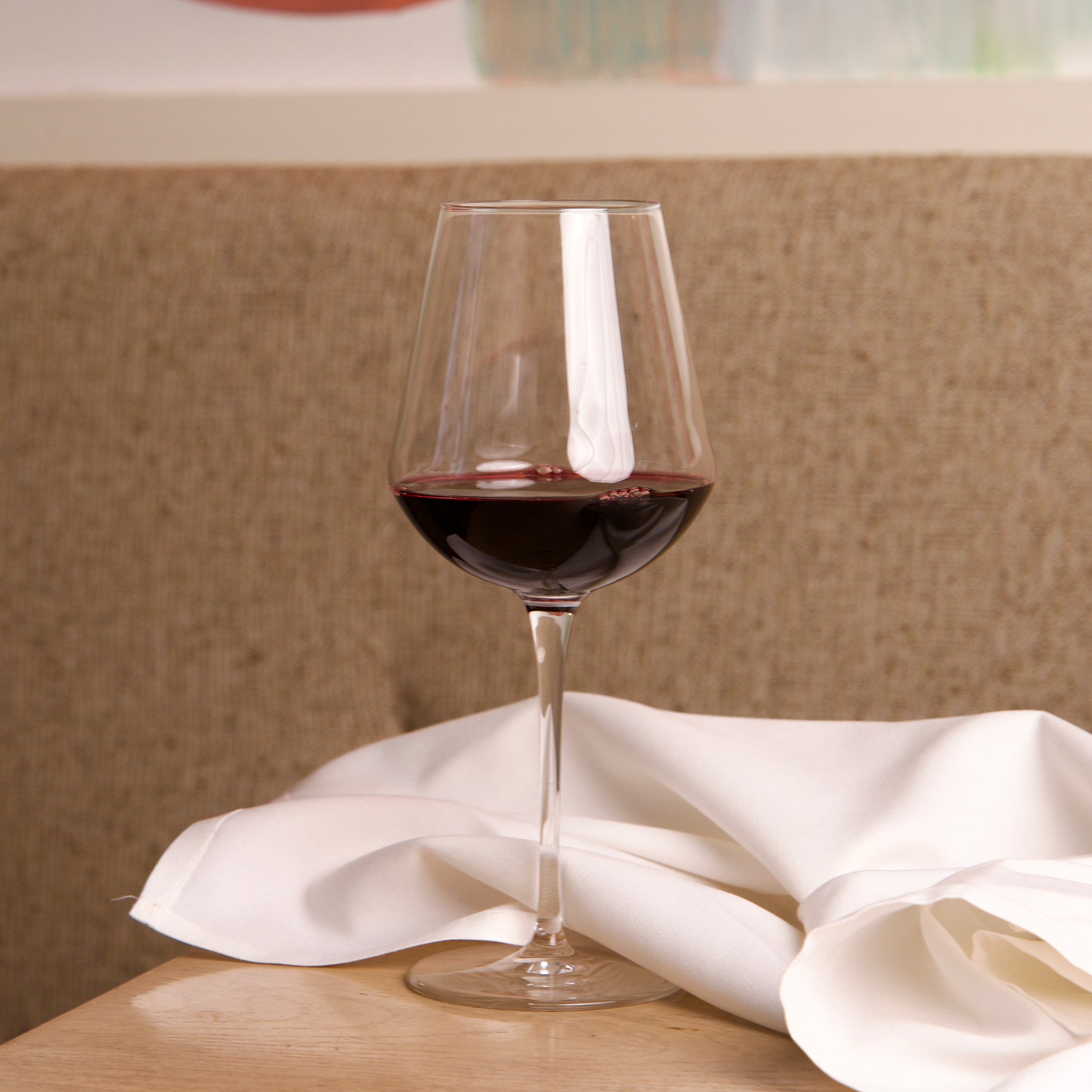 Glass of red wine on a wooden table with a white cloth, blurred background