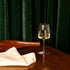 Planeo White Wine glass with white wine on a wooden table against a dark green curtain.