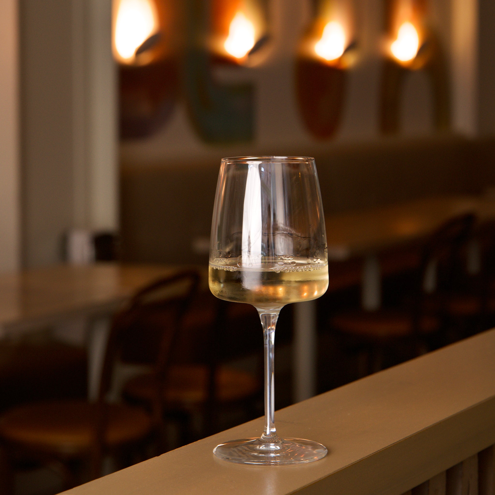 Glass of white wine on a bar counter with a blurred restaurant interior in the background