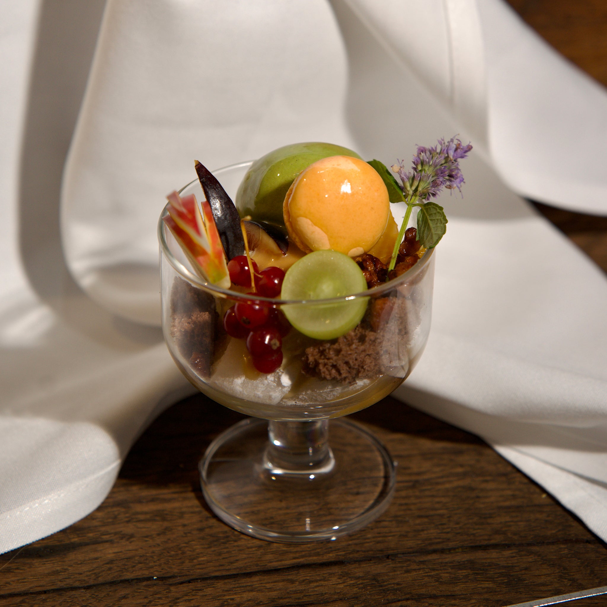Dessert in a glass bowl with fruits and a flower on a wooden surface